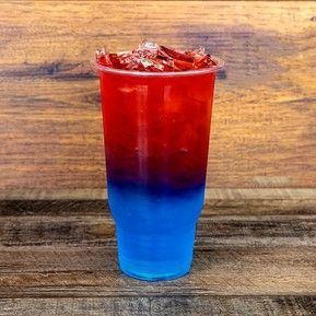 A red and blue drink in a plastic cup on a wooden table.