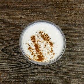 A cup of milk with cinnamon on a wooden table.