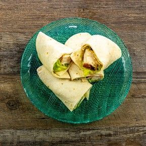 Three chicken wraps on a green plate on a wooden table.