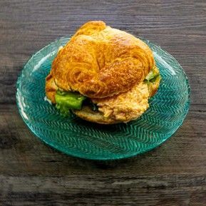 A sandwich on a croissant on a blue plate on a wooden table.