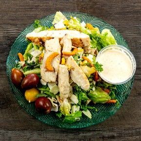 A salad with chicken , lettuce , carrots , tomatoes and dressing on a plate.