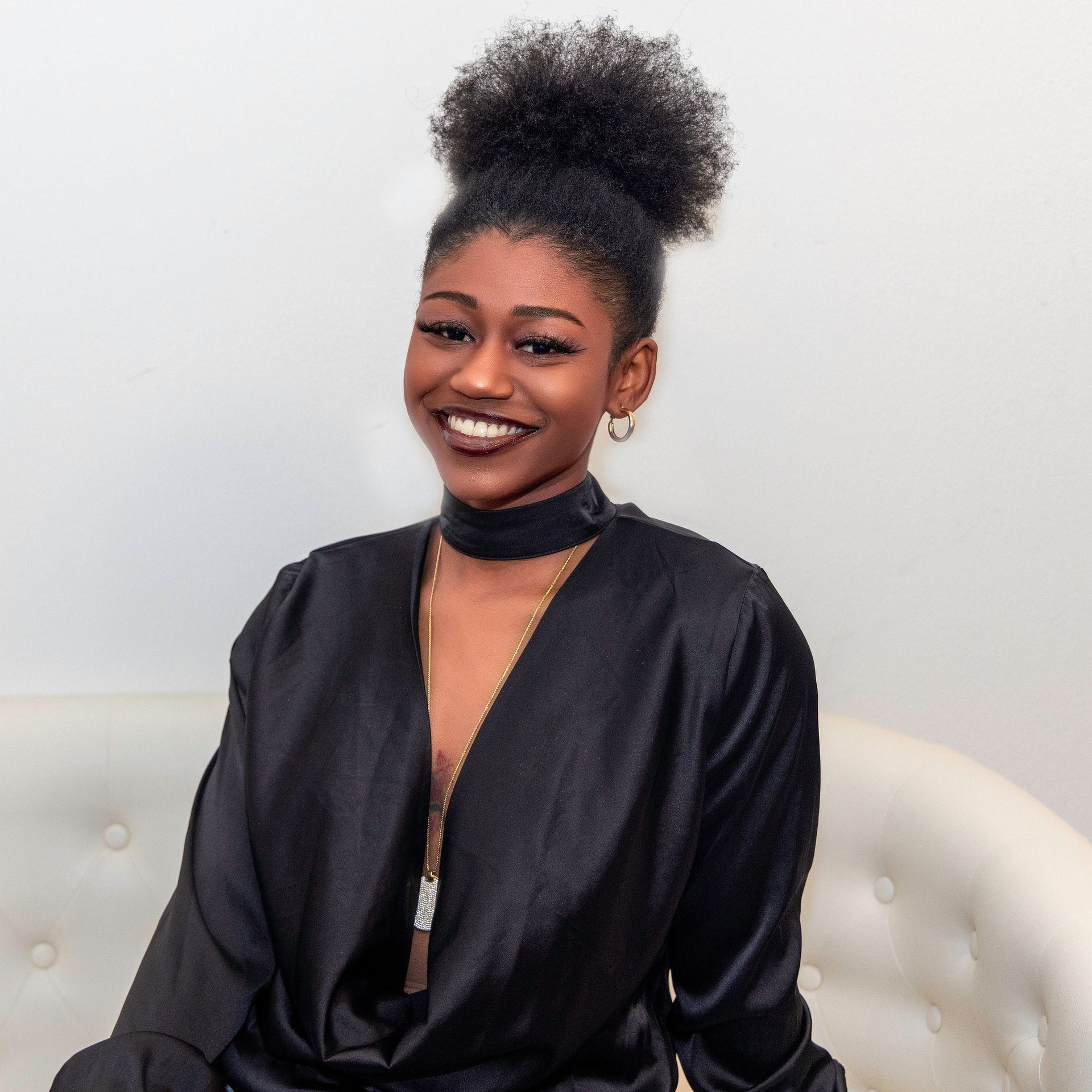 A woman in a black dress is sitting on a couch and smiling
