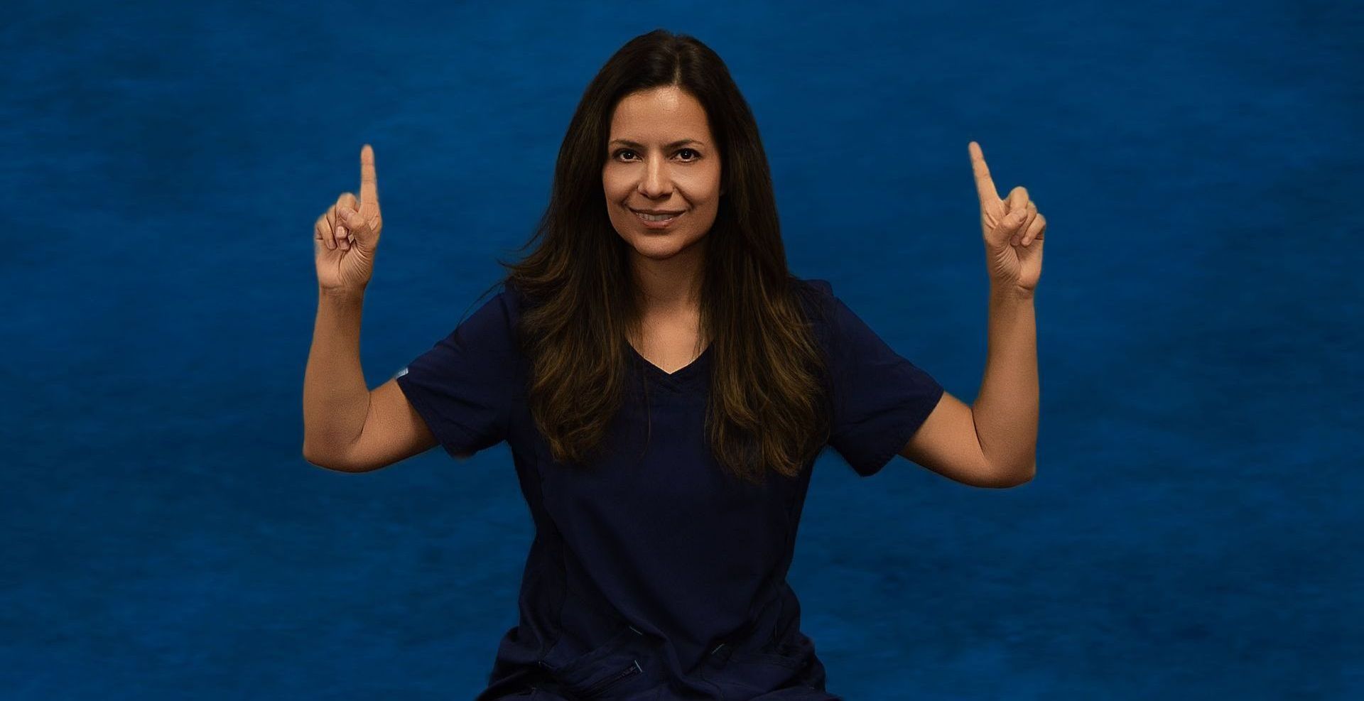 A woman is pointing up with her fingers in front of a blue background.