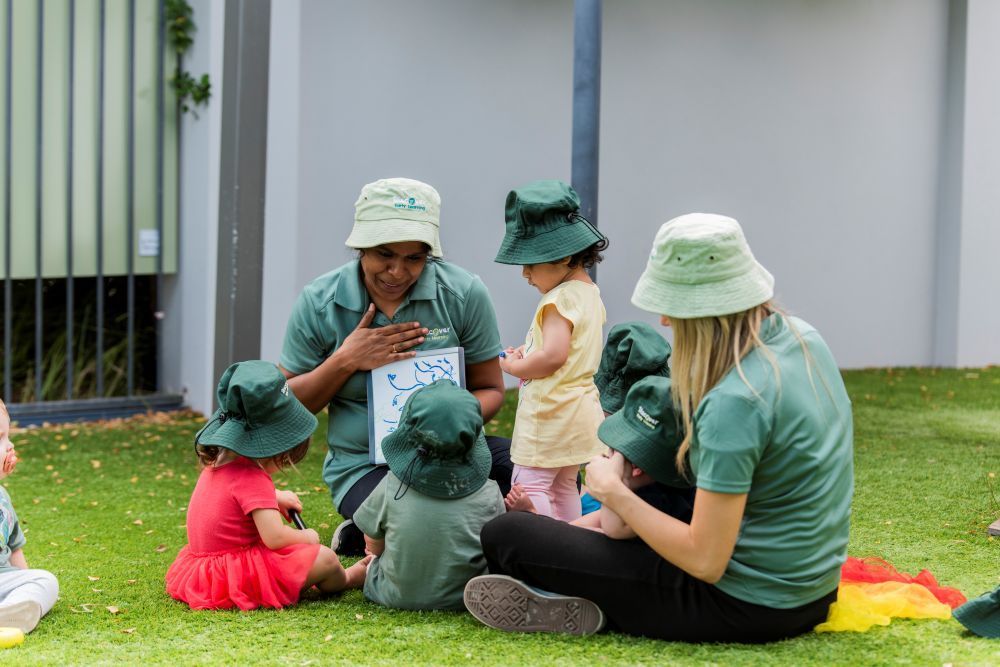 A group of children are sitting on the grass with a teacher  at Discover Early Learning.