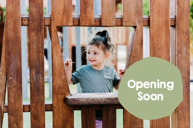 A little girl is looking out of a wooden fence  at Discover Early Learning.