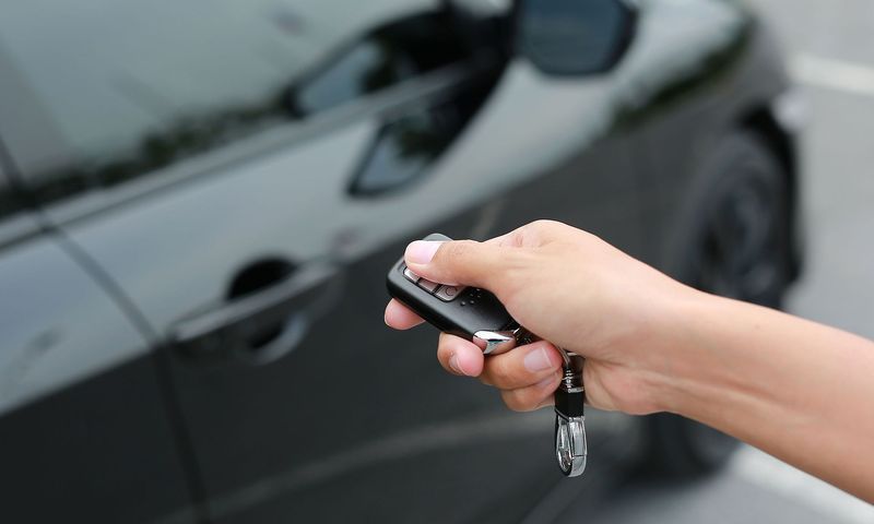 A person is holding a remote control in front of a car.