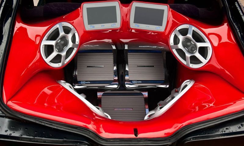 The trunk of a red car with speakers and two monitors
