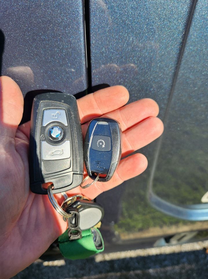A person is holding two car keys in their hand in front of a car.
