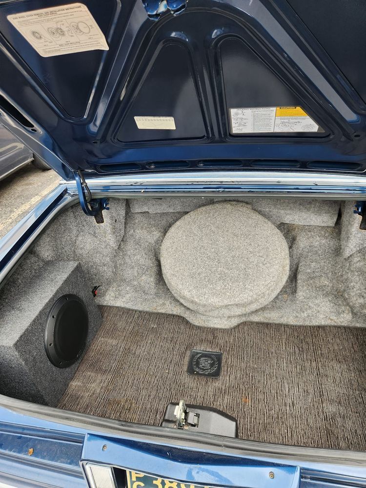 The trunk of a blue car with the hood open.