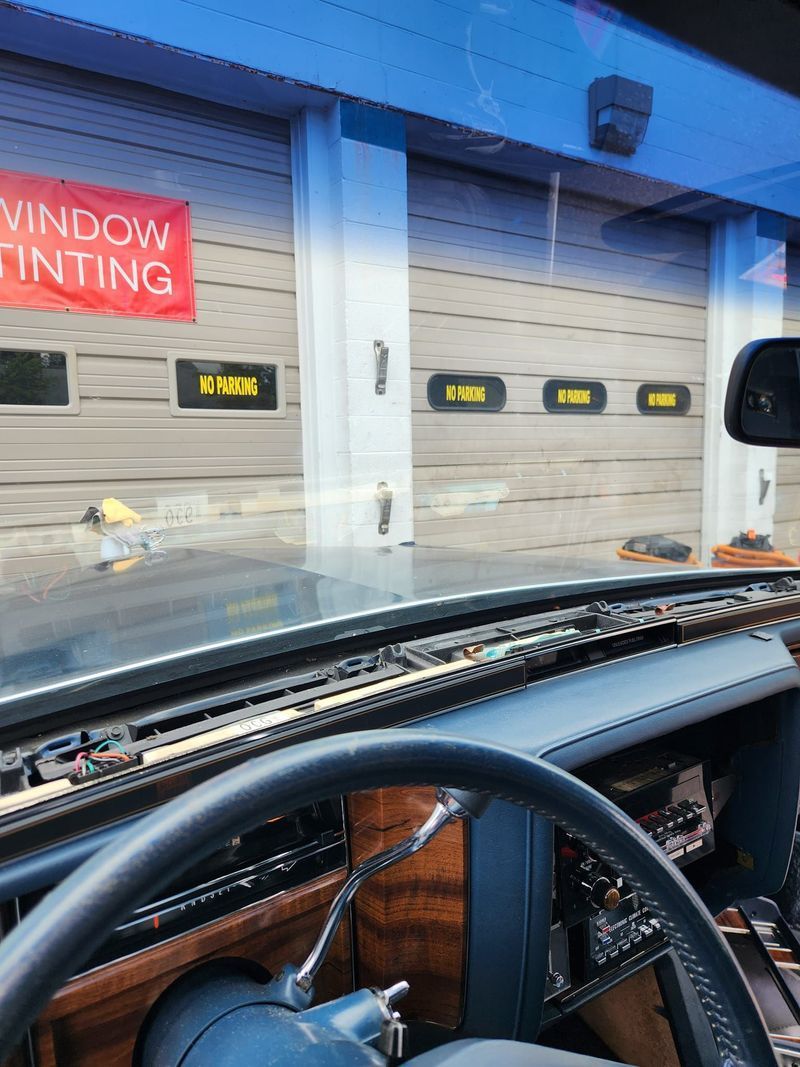 A car is parked in front of a garage with a sign that says window tinting.