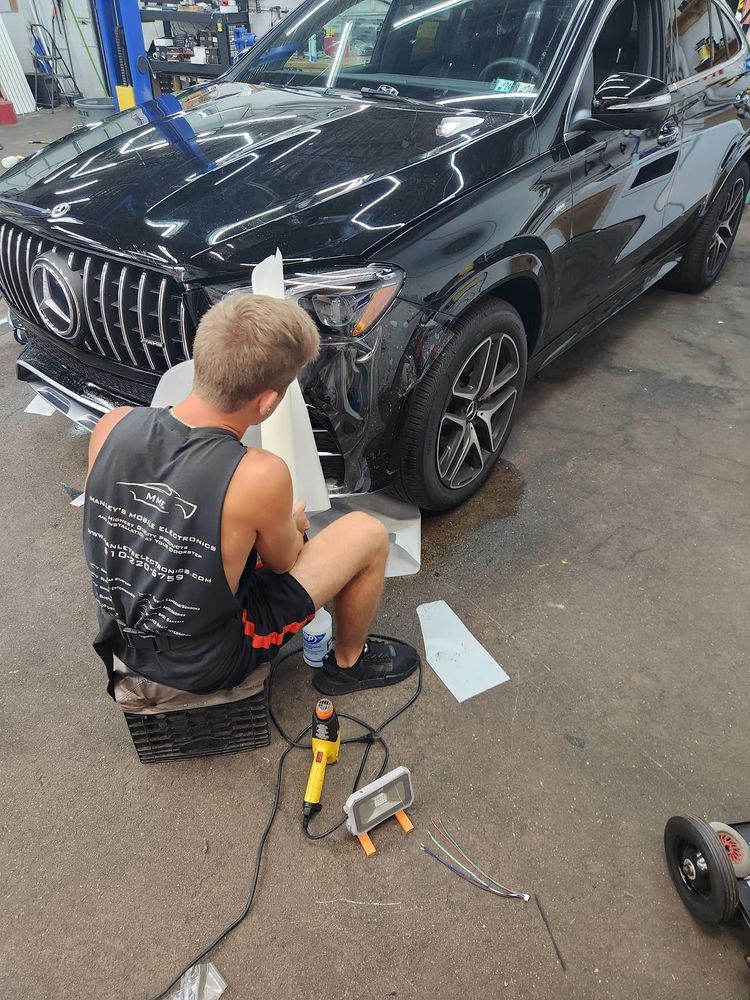 A man is sitting on the ground in front of a black car.