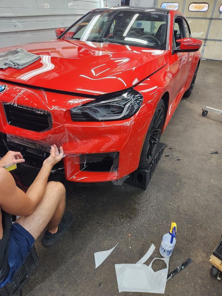 A man is applying a protective film to the front of a red car.