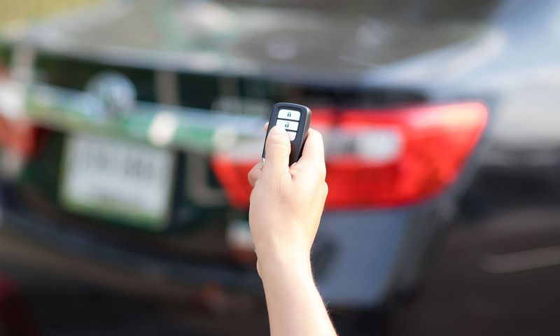 A person is holding a remote control in front of a car.