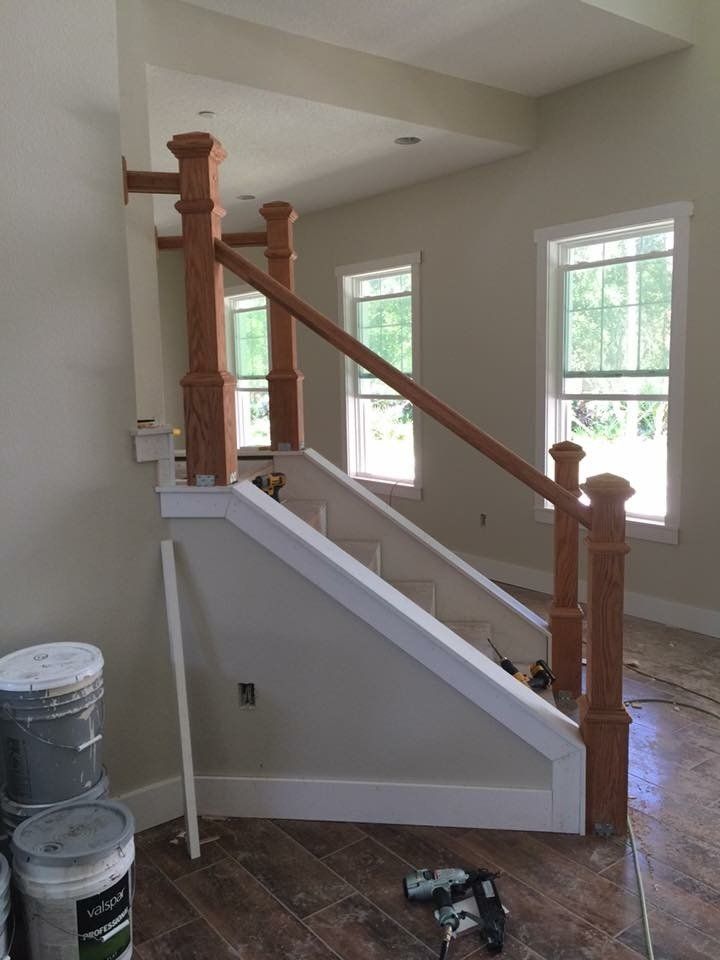 Interior view of a staircase with wood posts and a railing, near windows with natural light, construction in progress.