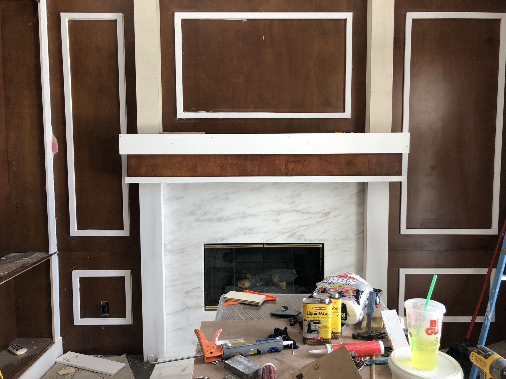 Fireplace with dark wood paneling, white trim, and a marble hearth, construction tools on the floor.