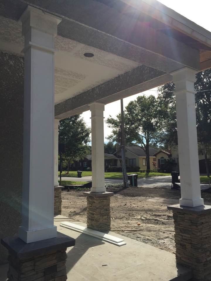 White porch columns with stone bases and a view of a street and trees in the background.
