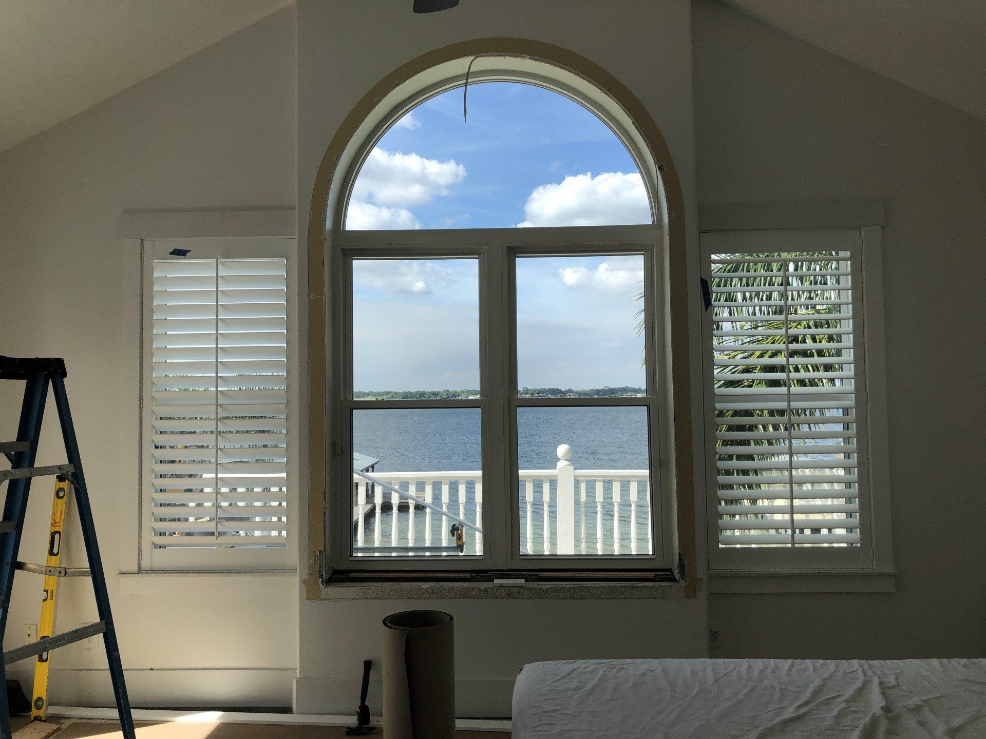 Interior room with three windows. Central arched window overlooks water, side windows have shutters.