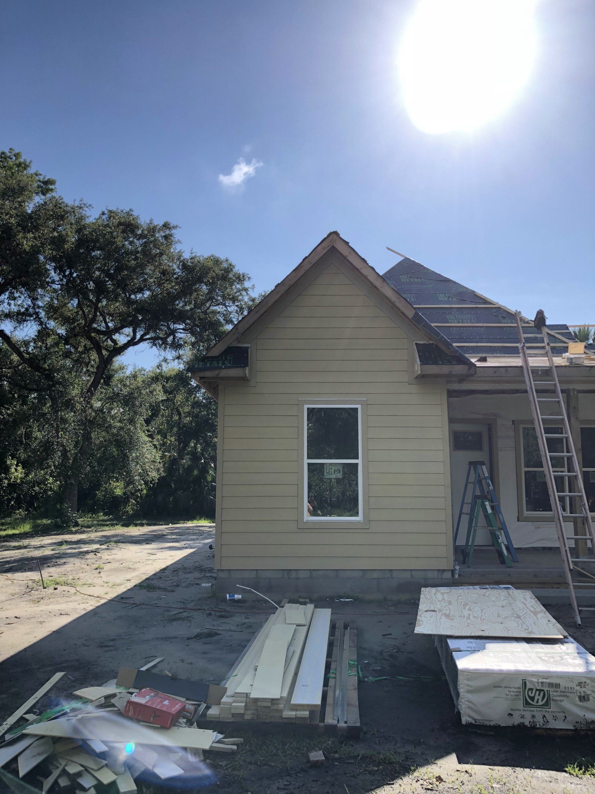 Construction of a house on a sunny day. Side view of beige siding and gabled roof, materials in foreground.