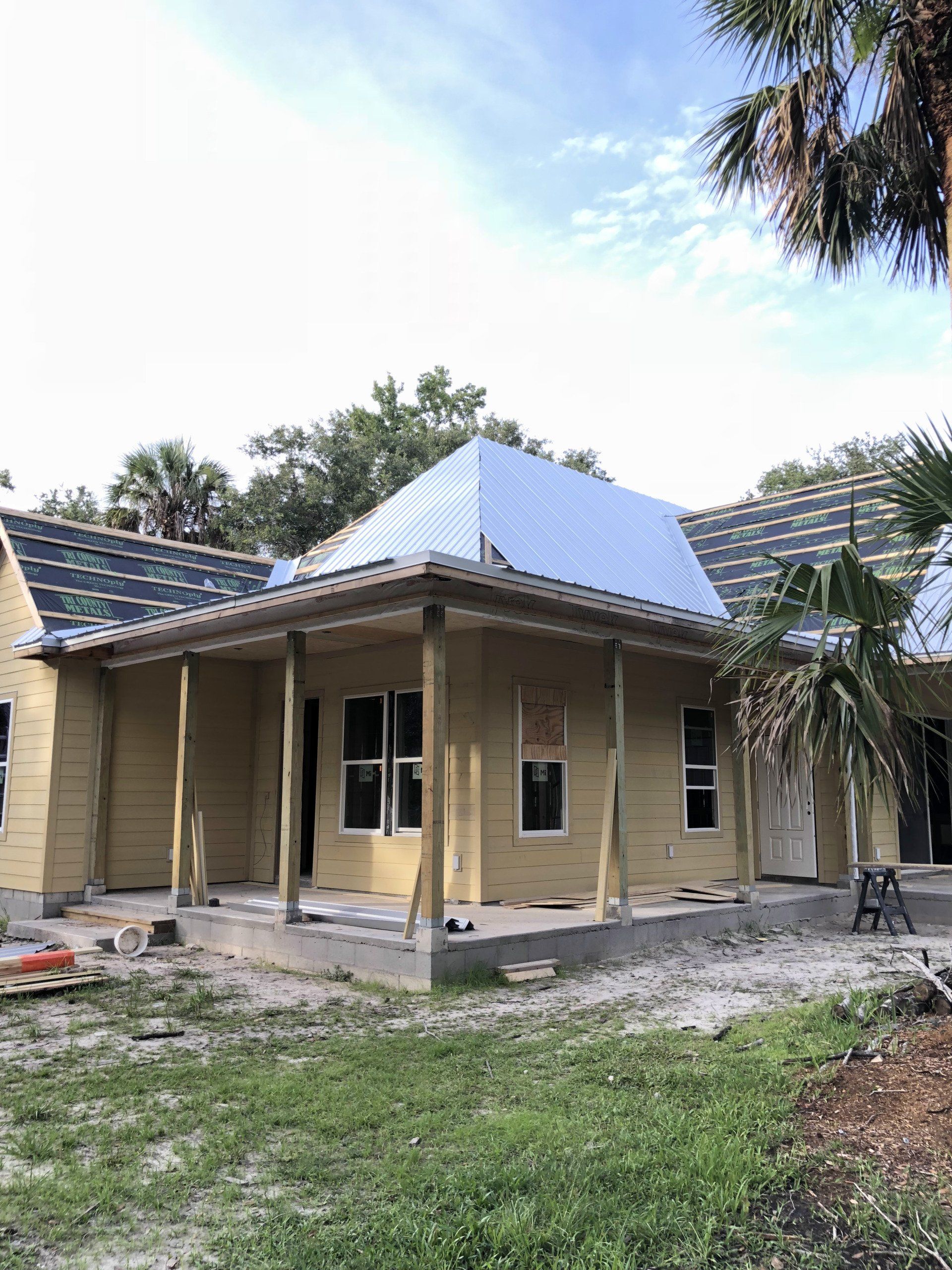 Yellow house under construction with porch and partially shingled roof.