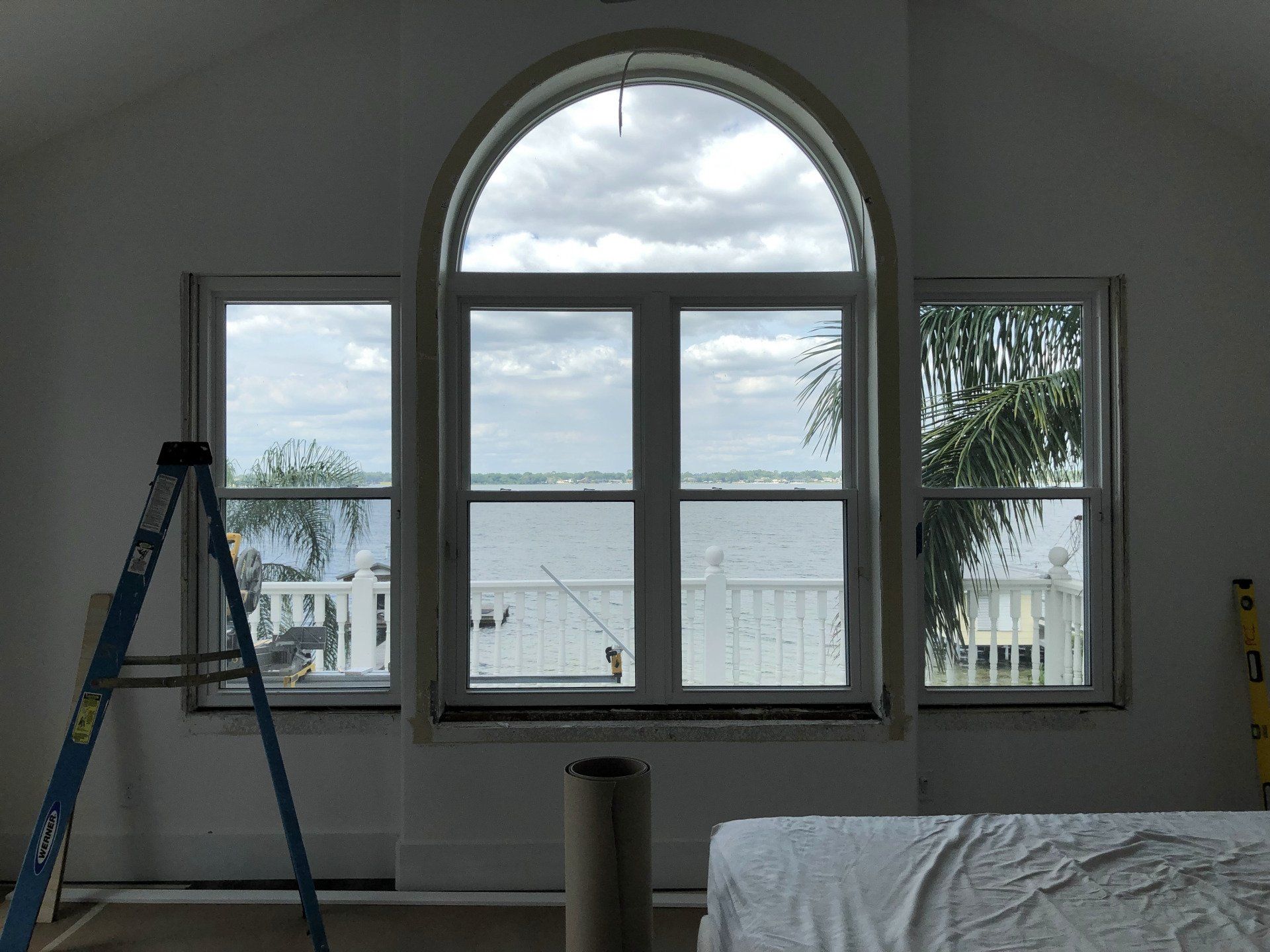 Interior view with three windows overlooking water; a ladder and roll of material are in the room.
