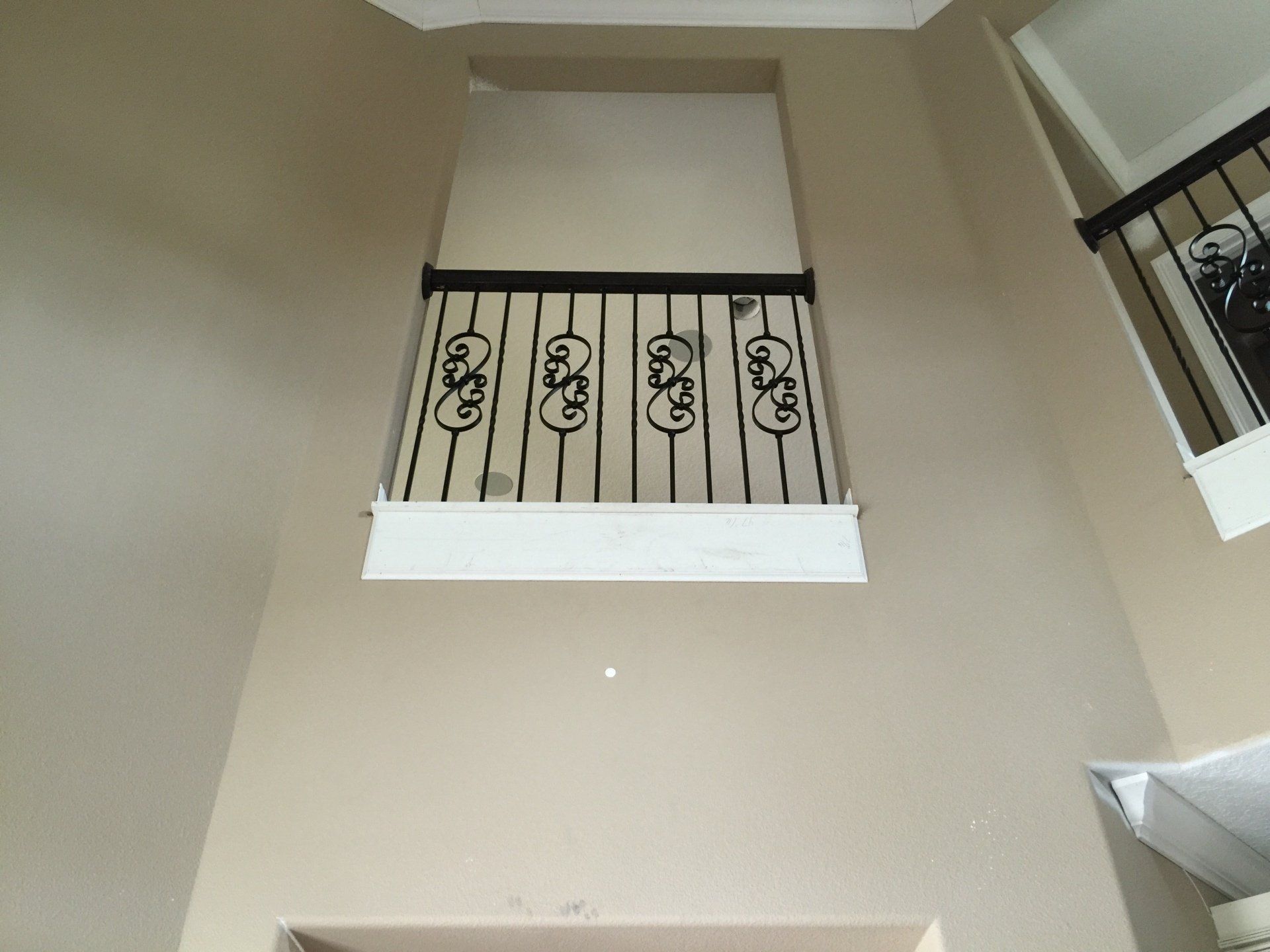 Interior view of a balcony with black metal railing, against a beige wall.