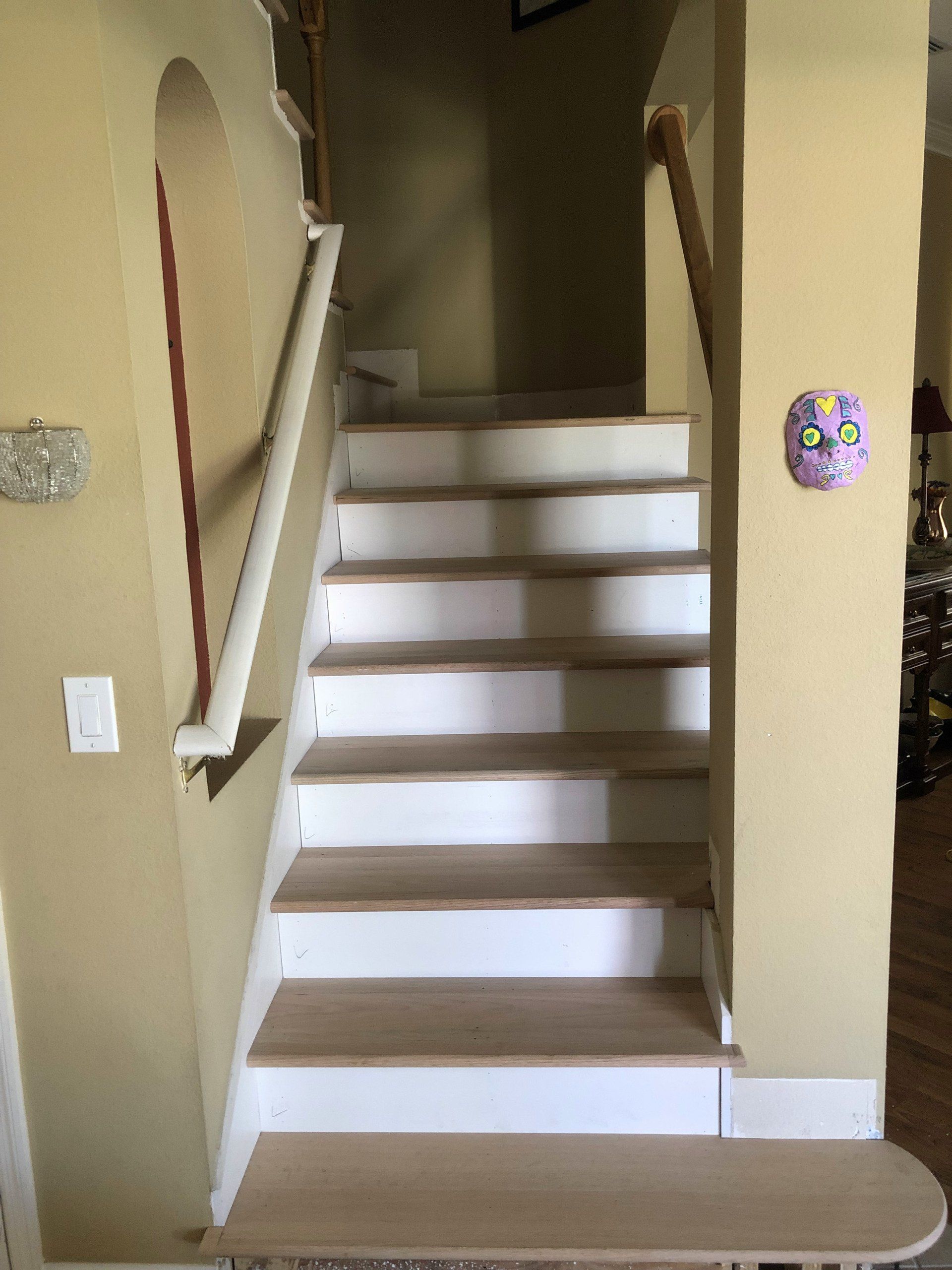 Staircase with light-colored steps, white risers, and a handrail. A decorative mask hangs on the wall.