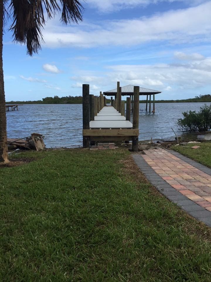 Dock extending into a body of water with blue sky and palm tree.