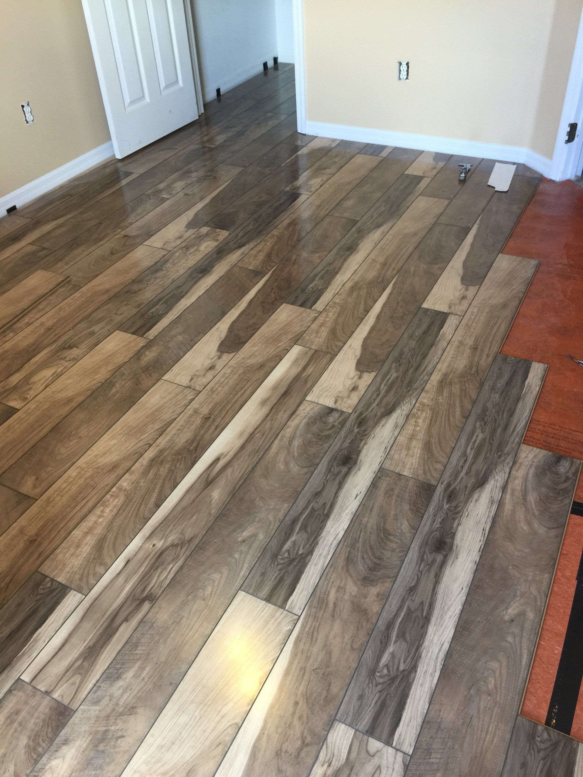 Wooden floor planks being installed in a room with tan walls and a white door.
