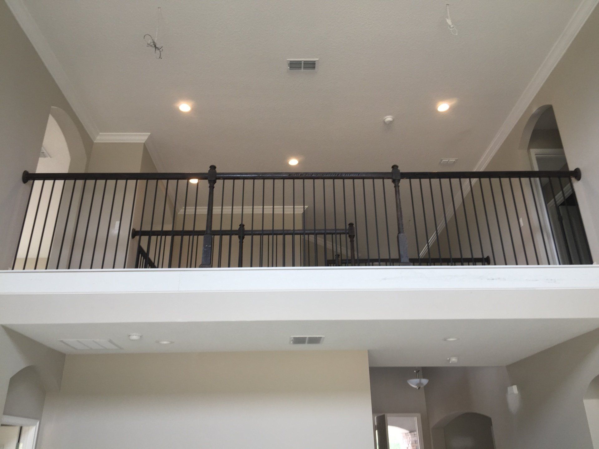 Interior view of a two-story home with a black railing, overhead lighting, and beige walls.