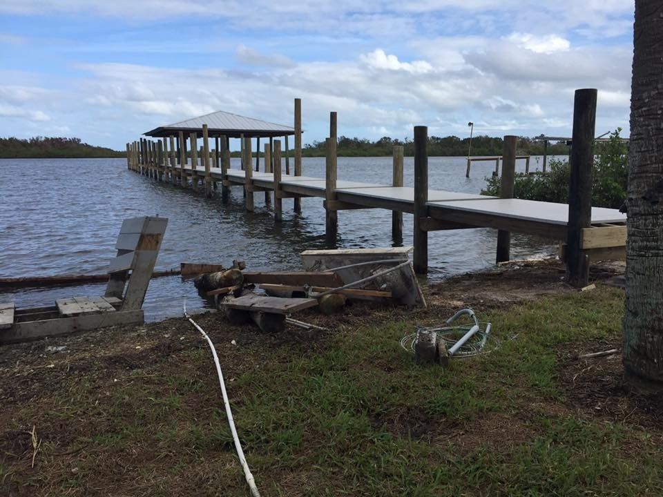 Dock extending into water, with covered seating area at end. Cloudy sky, grassy foreground.