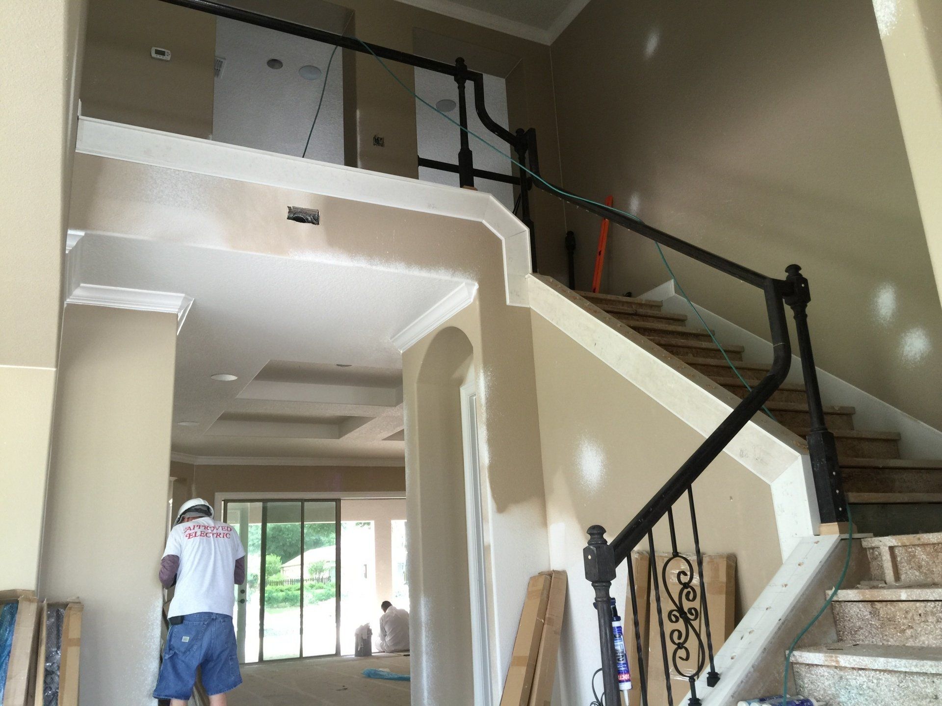 Interior view of staircase with black railing, beige walls, and a person working on the wall.