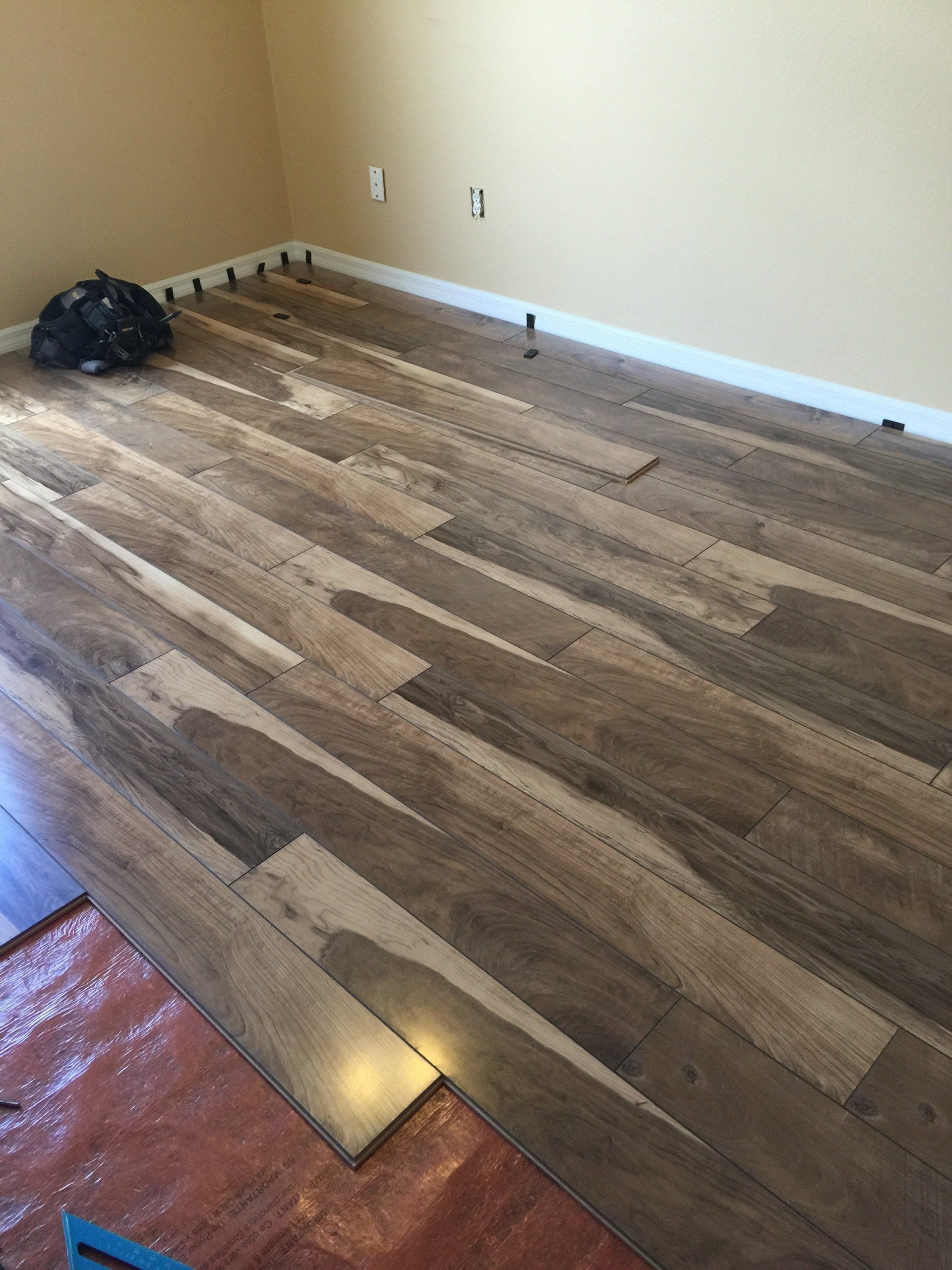 Installing laminate flooring in a room with beige walls. Wooden planks are being laid on the floor.