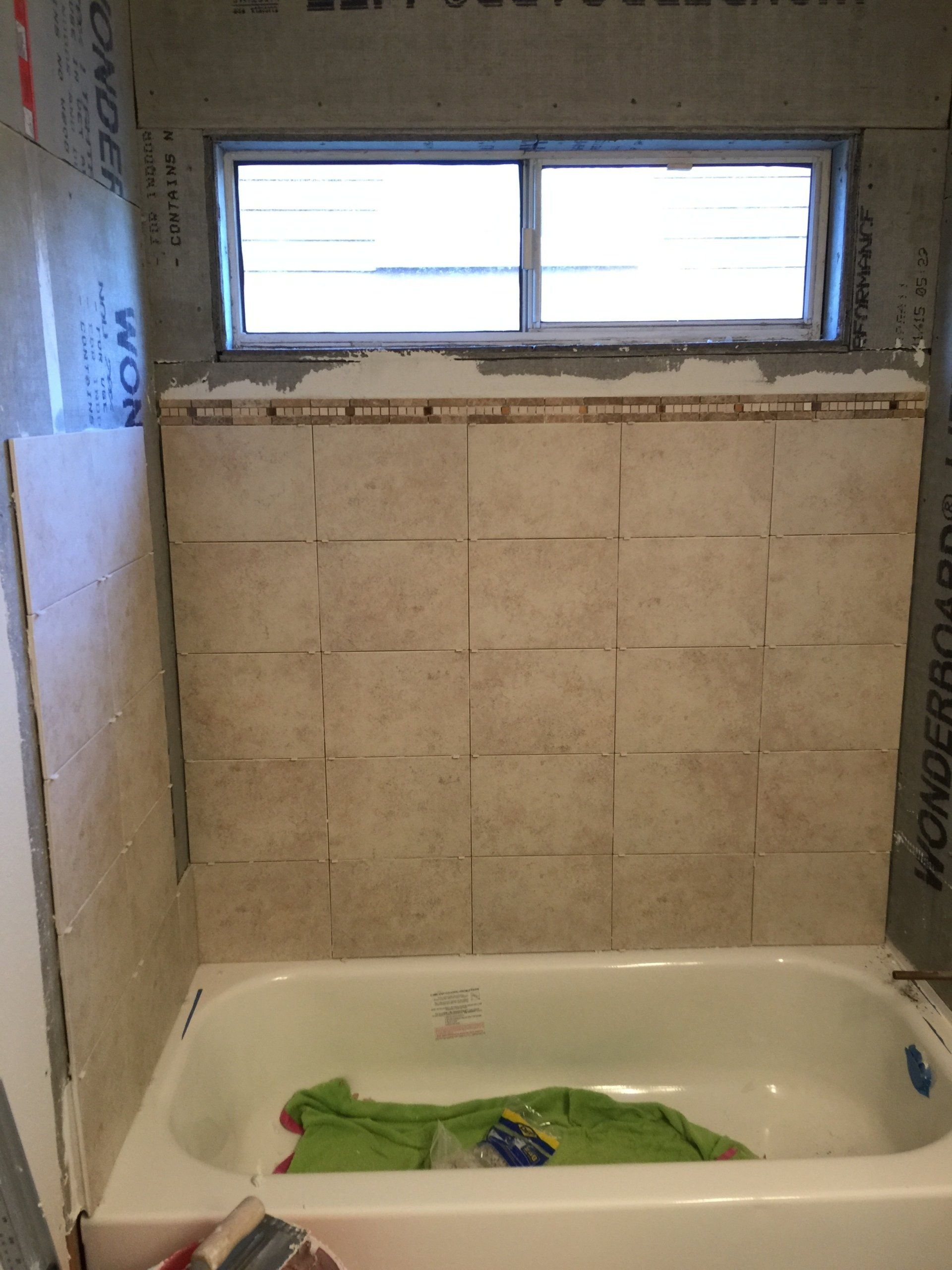 Bathroom with tan tiles above a white tub, with a window and decorative border tiles.