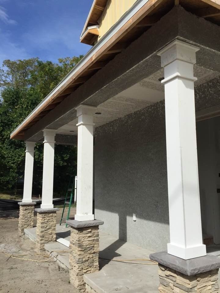 Exterior view of a building under construction, featuring white pillars with stone bases and a covered porch.