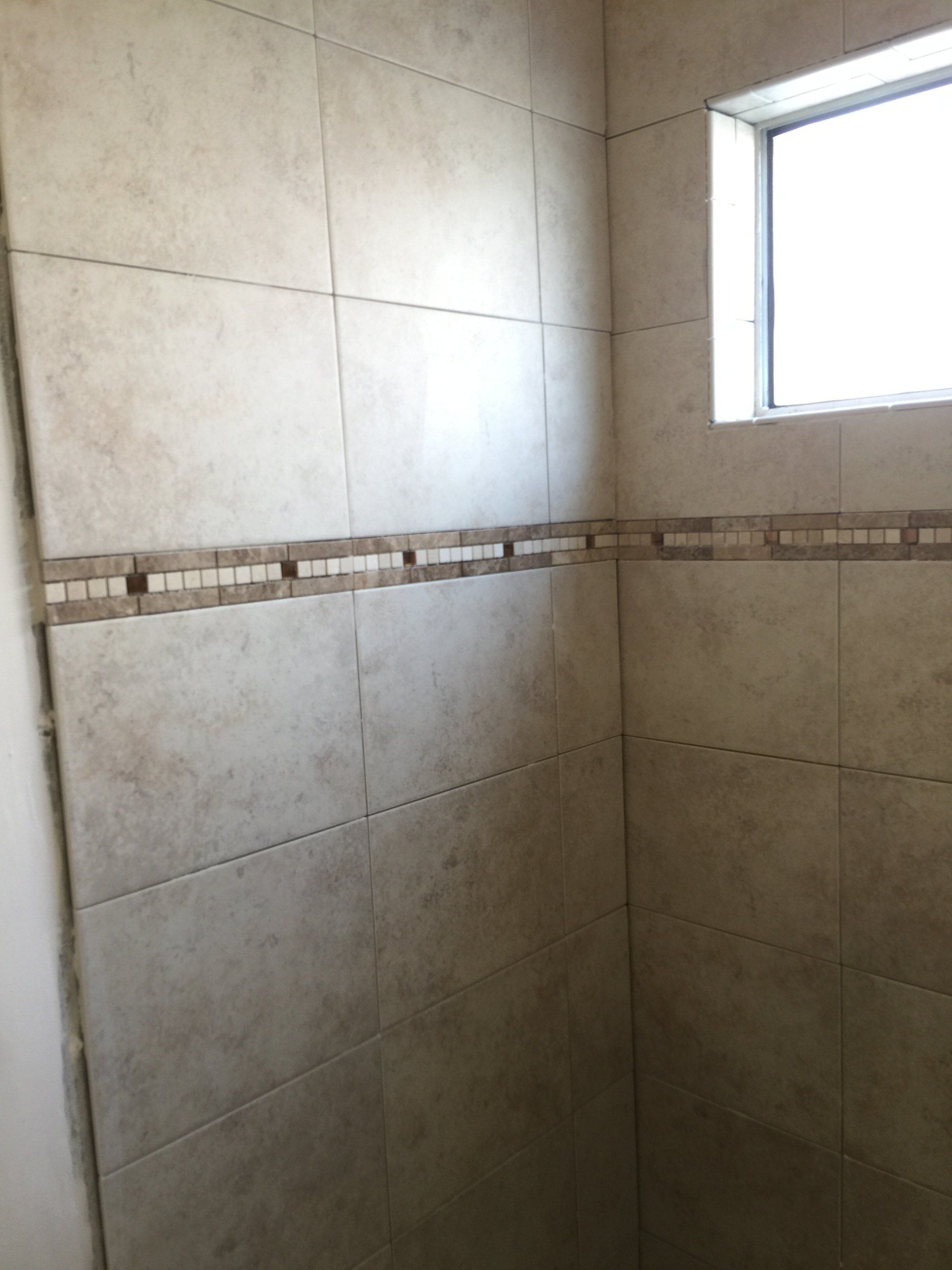 Beige tiled shower with a decorative border and a window.