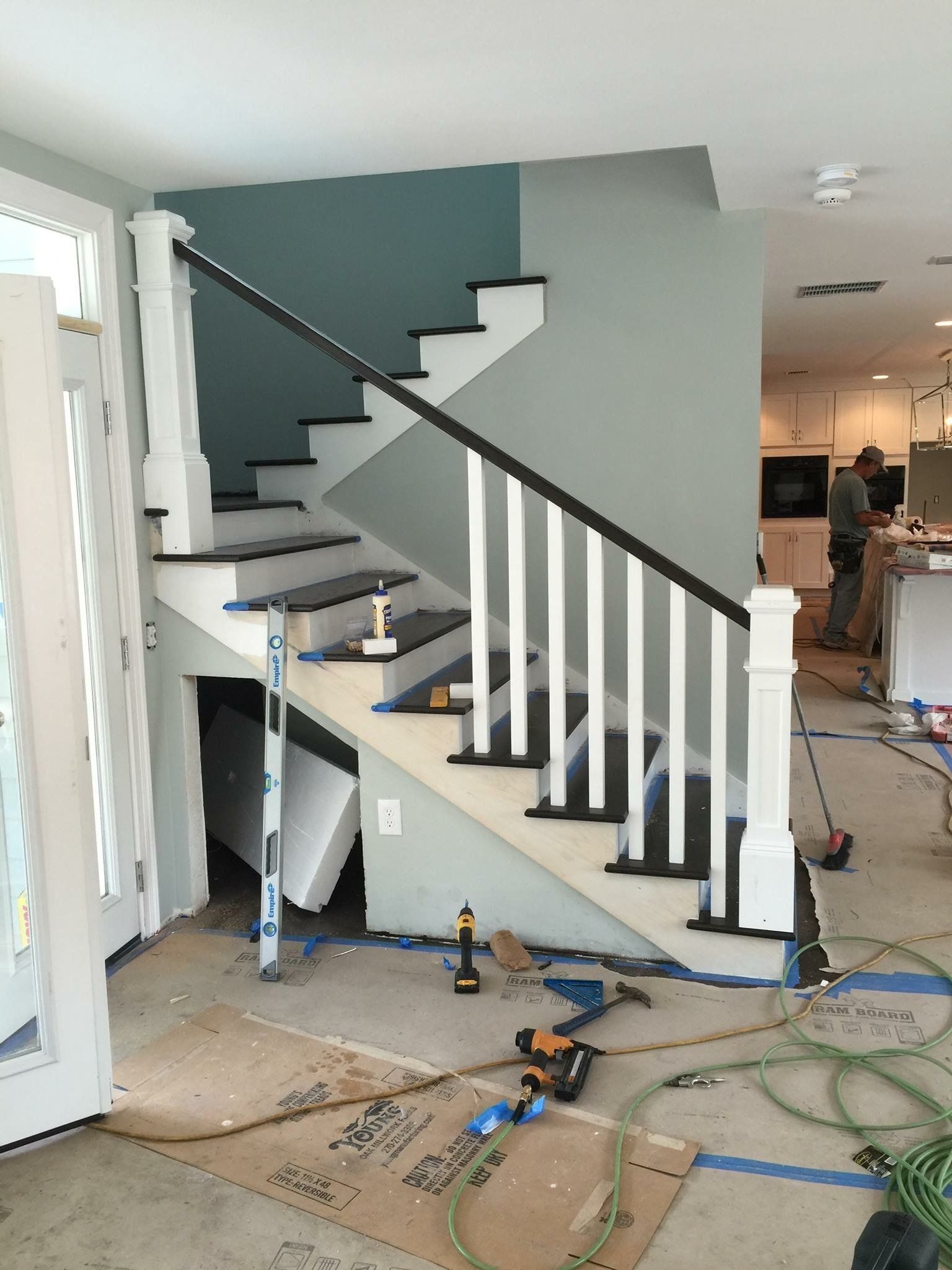 Staircase with white railing, black treads, and blue-green accent wall; construction tools on floor.