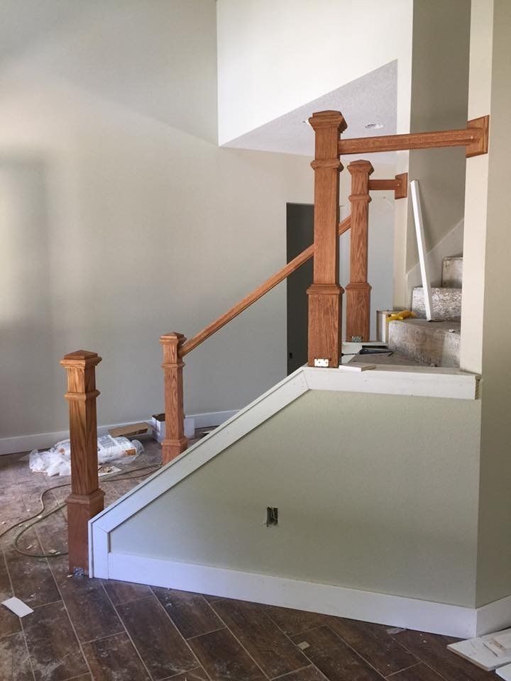 Staircase under construction with wooden balusters, handrail, and trim. Light green and white walls; brown flooring.