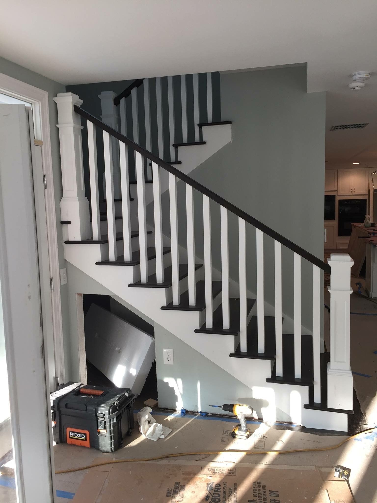 White and black staircase with vertical white spindles, gray wall, construction tools visible.