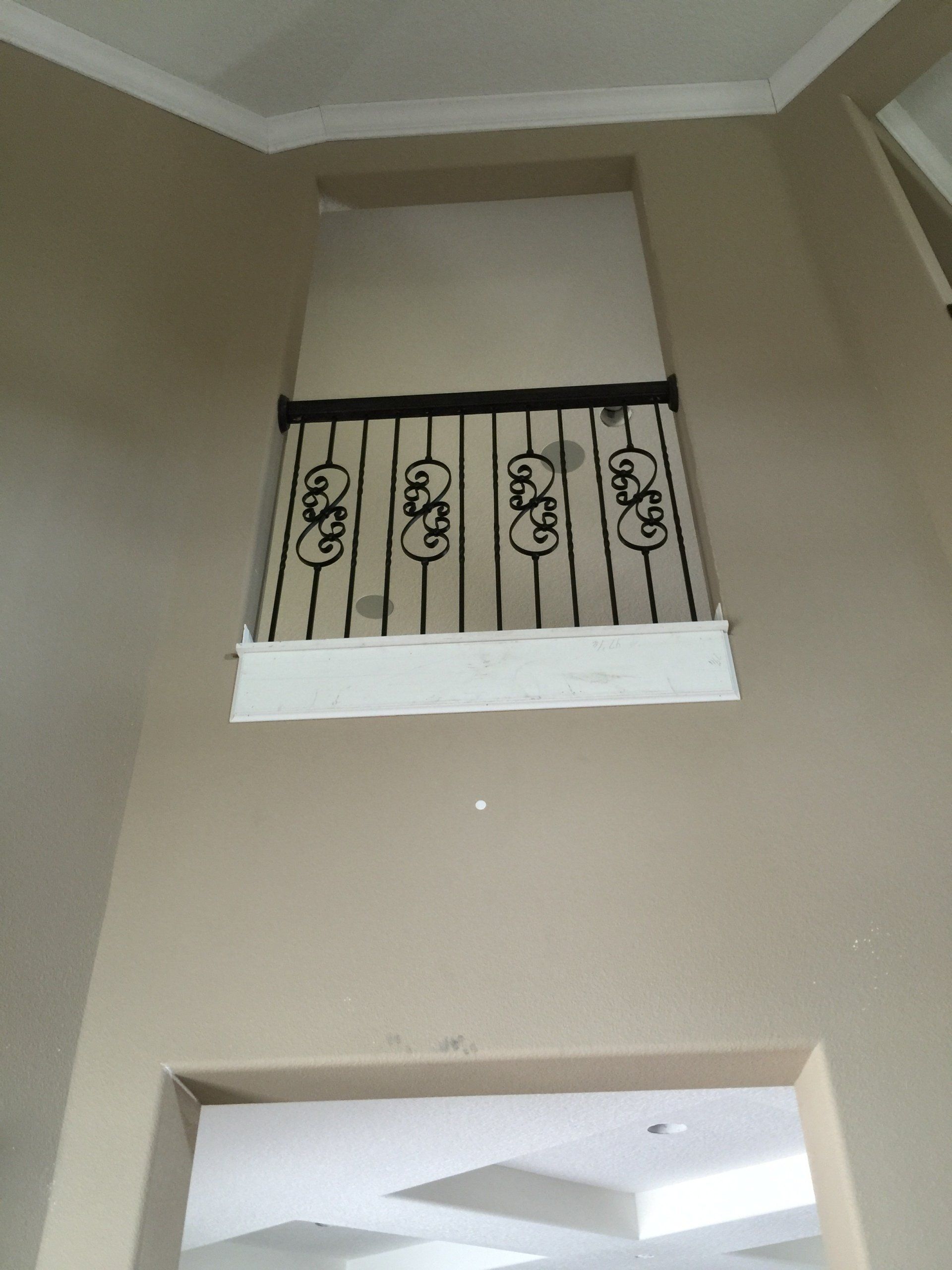 Interior view of a high-ceilinged room with a balcony featuring decorative black railing. Beige walls.
