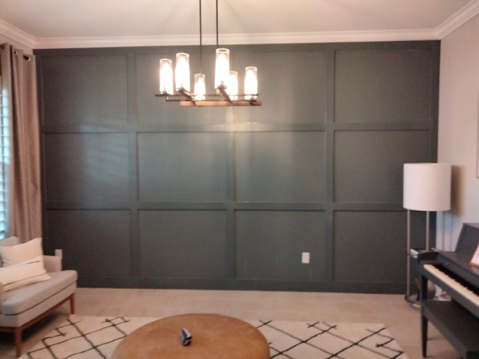 Dark gray paneled accent wall with a modern chandelier, armchair, and piano.