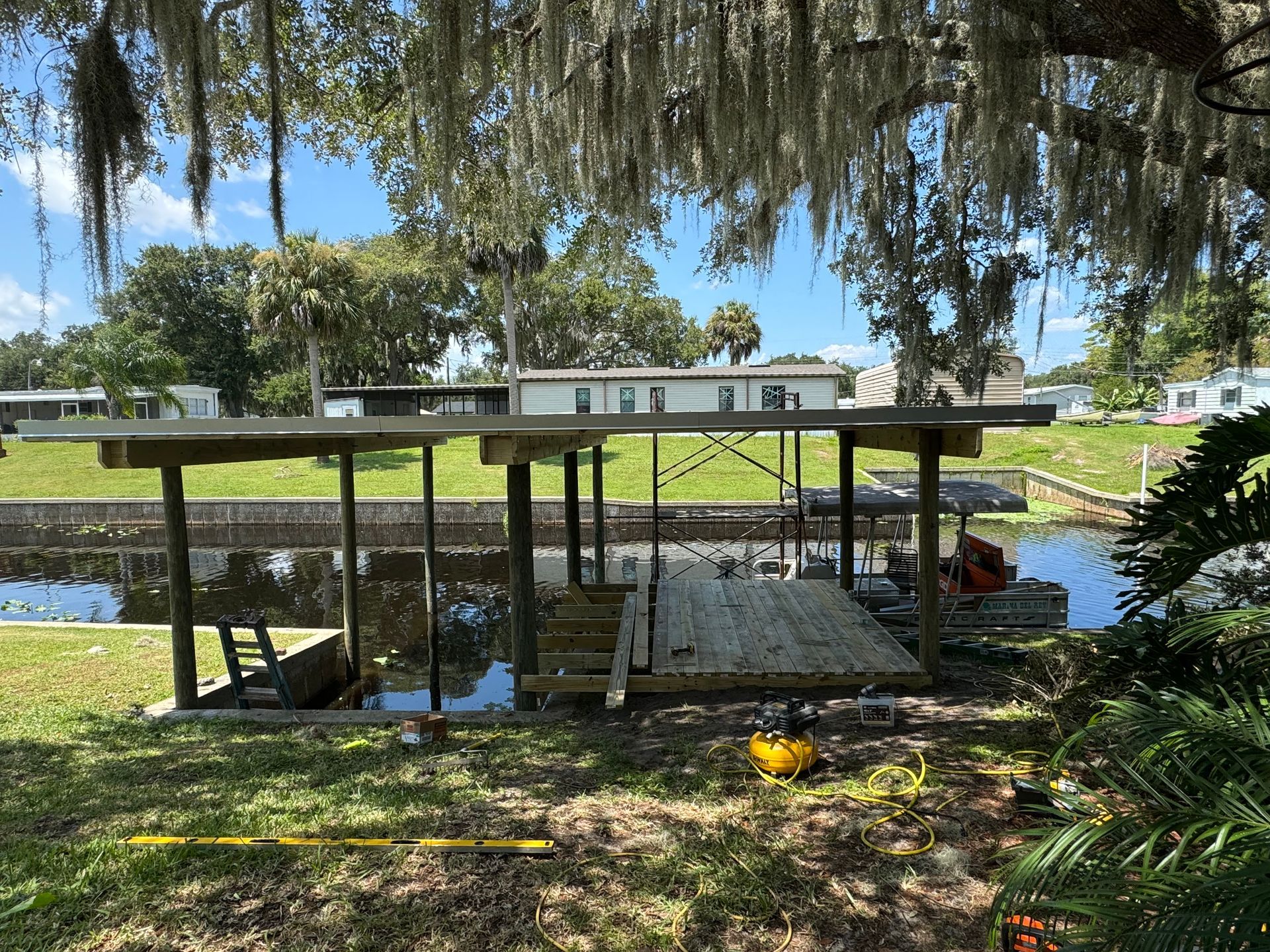 Wooden boat dock on a canal under a tree with Spanish moss; houses in background.