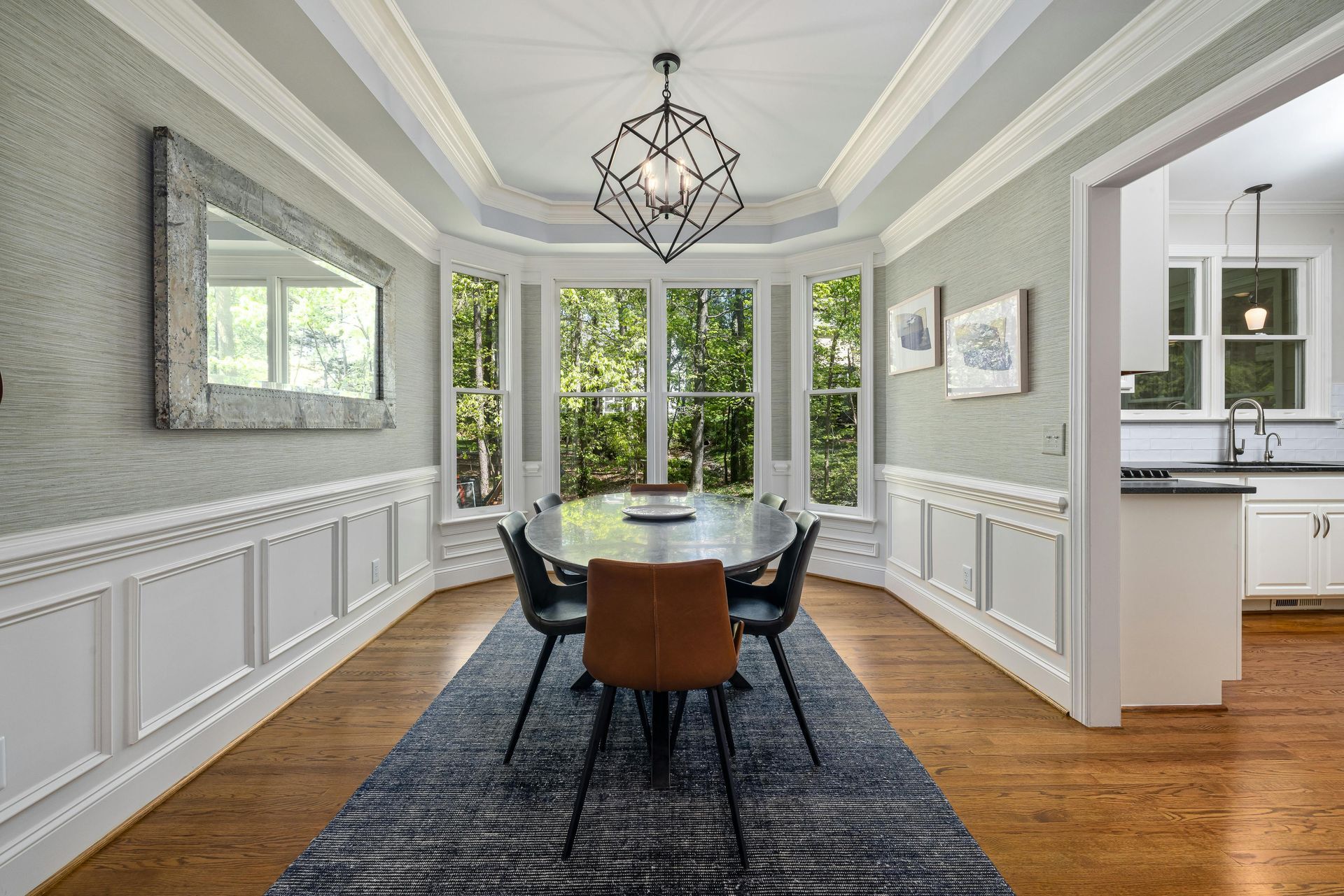 Dining room with oval table, chairs, and bay window. Gray walls, white trim, and a patterned rug.