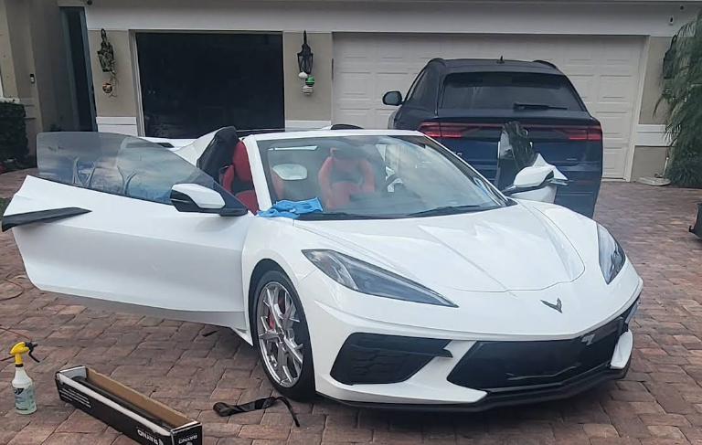 White convertible sports car with red interior, parked in a driveway. The door is open.