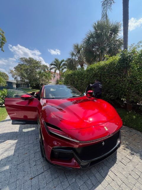 Red Ferrari SUV parked on a brick driveway, door open, sunny day.