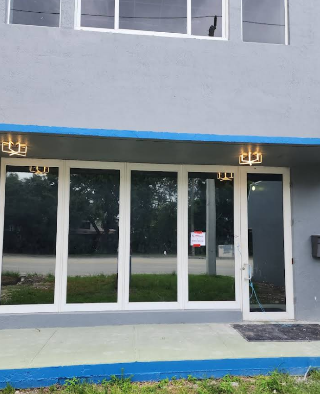 Building entrance with large windows, gray facade, two wall sconces. 