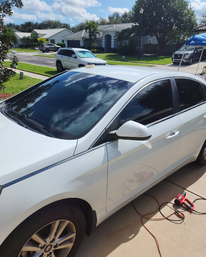 White sedan with tinted windows parked on a driveway in front of suburban houses.