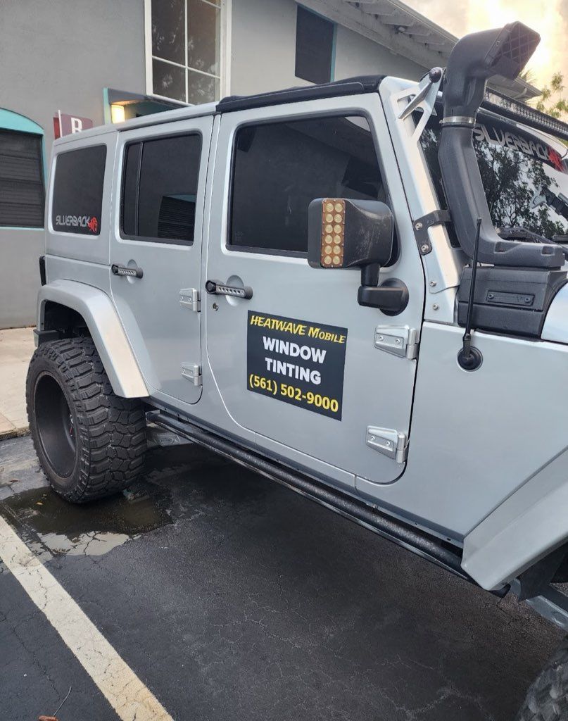 Silver Jeep with tinted windows, black tires, and a business advertisement on the door.