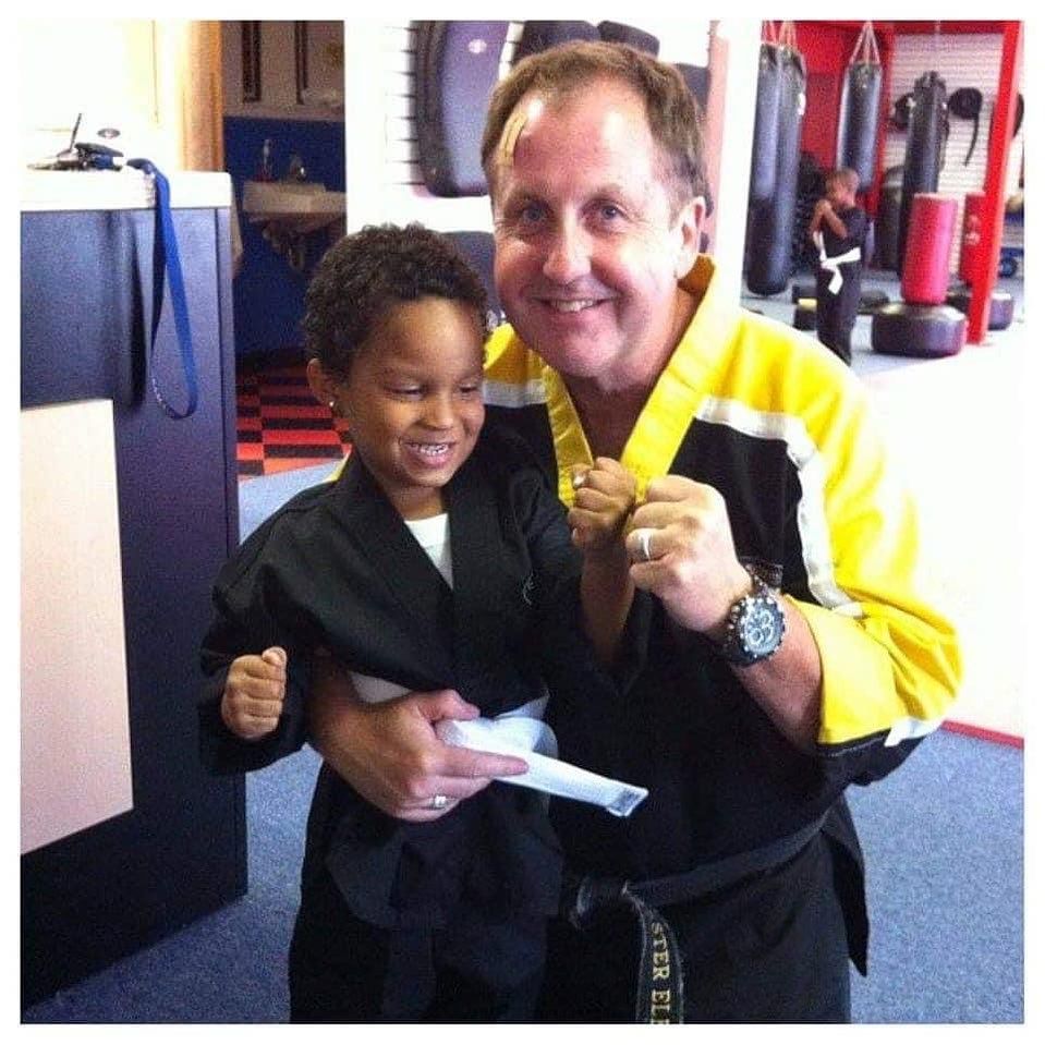 A man in a yellow jacket holds a young boy in a black karate uniform