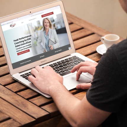 close up of man's hand typing on a laptop that shows the homepage of 3-by-5 Coaching's website, with a smiling blonde woman on the screen