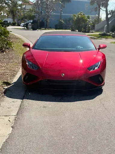 Red Lamborghini Huracan parked on a road. Bright sunlight, residential setting.